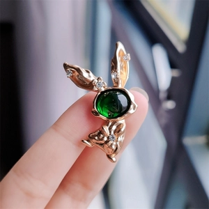 Macro shot of gold rabbit brooch featuring a large green gemstone and white zircons
