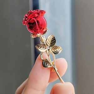 Détail macro d'une broche rose en émail rouge avec feuilles dorées tenue à la main