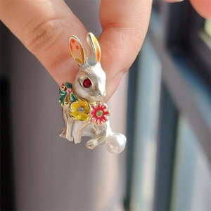 Macro detail of silver rabbit brooch with enamel flowers and a large pearl accent