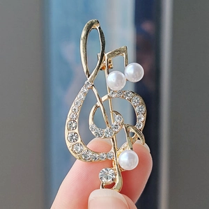 Detailed close-up of golden treble clef brooch with sparkling rhinestones and white pearls