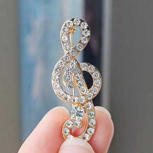 Macro shot of gold-plated treble clef brooch with sparkling rhinestones held by hand