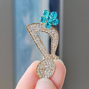 Macro shot of musical note brooch with inlaid white crystals and blue floral detail