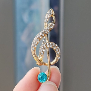 Detailed close-up of a gold treble clef brooch with white crystals and a blue gemstone