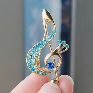 Detail of music note brooch with gold plating and blue rhinestones held by hand
