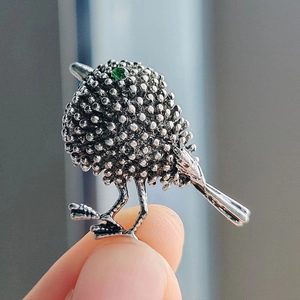 Vintage silver sparrow brooch featuring textured wings and a striking green gemstone eye
