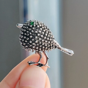 Vintage bird brooch in silver metal with textured beadwork and a green gemstone eye