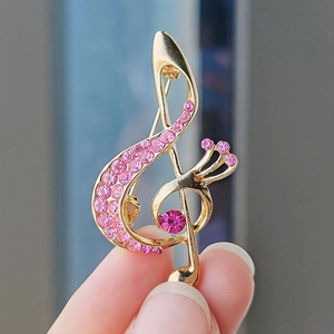 Golden musical note brooch with pink rhinestones shown in a detailed close-up shot