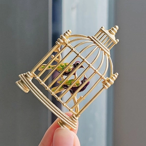 Vintage gold birdcage brooch featuring colorful enamel birds and intricate relief design