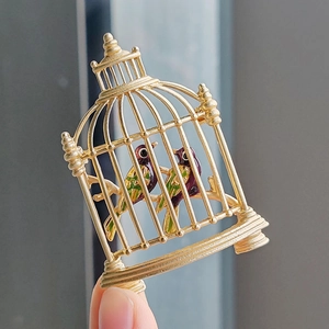 Vintage gold birdcage brooch with colorful enamel birds shown in a hand-held view