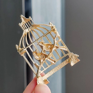 Vintage gold metal birdcage brooch with twin birds design and secure pin closure