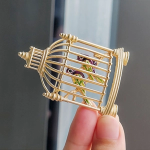 Close-up of vintage golden birdcage brooch with colorful enamel birds held in hand