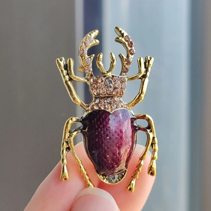 Vintage beetle brooch with gold base and purple enamel detail held in natural light
