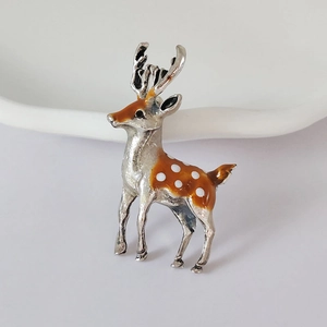 Detailed view of silver deer brooch featuring orange enamel finish and white polka dots