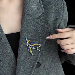 Close-up of blue and yellow enamel swallow brooch on a grey tweed suit lapel