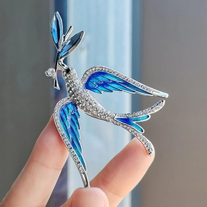 Detailed close-up of blue enamel swallow brooch with sparkling crystals and olive branch