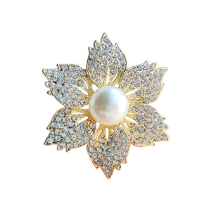 Élégante broche fleur dorée avec six pétales en strass et une perle centrale sur fond blanc