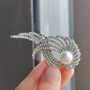 Dettaglio di un'elegante spilla a piuma con strass pavé e una grande perla bianca