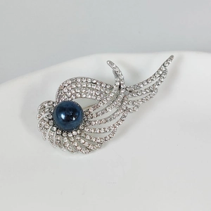 Dettaglio della spilla ad ali di angelo con strass bianchi e perla blu scuro centrale