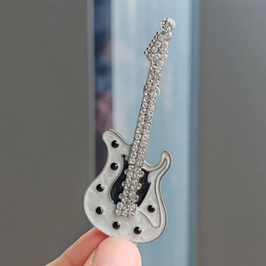Close-up of a silver electric guitar brooch with sparkling rhinestones and white pearlescent finish