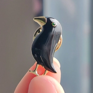 Detailed view of raven enamel brooch featuring golden beak and green rhinestone eye