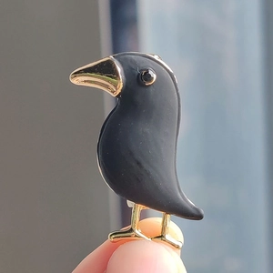 Minimalist black crow brooch with golden beak and legs shown in hand for size