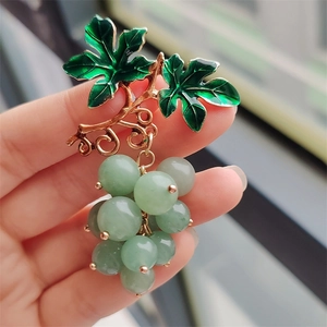 Macro detail of grape brooch showing green enamel leaves and translucent beads on golden stem