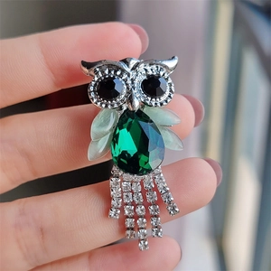 Detailed macro view of an owl brooch with emerald glass body and sparkling rhinestone tassels