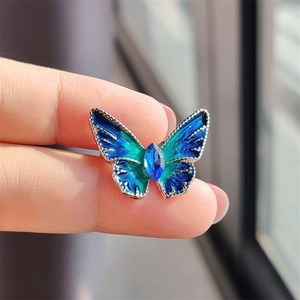 Detail van blauwe vlinderbroche met emaille verloop en centraal kristallen accent
