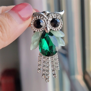 Detail of owl brooch with green gemstones, silver tassels, and crystal accents on hand