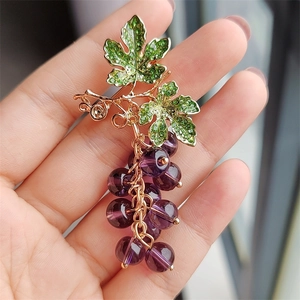 Detailed close-up of grape-shaped brooch with purple beads and green rhinestones in palm