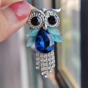 Detail of owl brooch featuring blue crystal teardrop and silver tassels held by hand