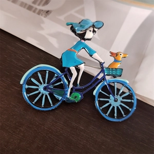 Détail de broche émaillée montrant une fille à vélo avec un petit chien dans le panier
