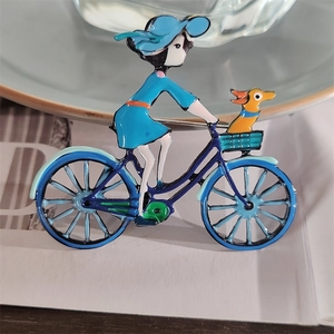 Détail macro d'une broche en émail représentant une fille à vélo avec un petit chien
