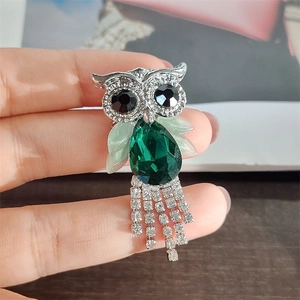 Detailed close-up of owl brooch with green crystal body and sparkling rhinestone tassels