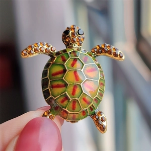 Close-up of a vintage tortoise brooch featuring green enamel and amber rhinestones