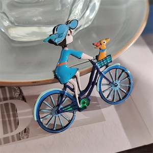 Détail de la broche émaillée fille à vélo avec finition bleue et petit chien