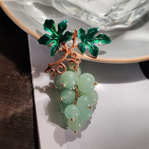 Detailed close-up of grape-shaped brooch with green enamel leaves and rose gold metal stem