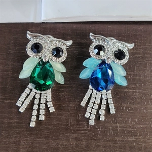 Close-up of owl brooches with crystal body and rhinestone tassels on wood