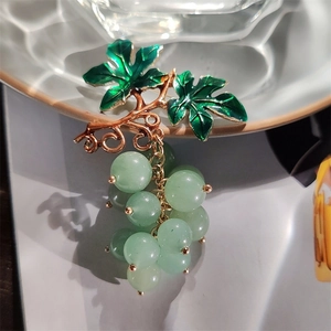 Elegant gold grape brooch with green enamel leaves and translucent beads on ceramic