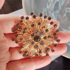 Macro shot of a vintage gold-toned floral brooch with grey rhinestones in hand