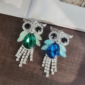 Detailed close-up of crystal owl brooch with emerald pear-shaped stone and tassel