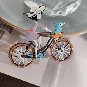 Détail de la broche en émail représentant une fille à vélo avec un petit chien