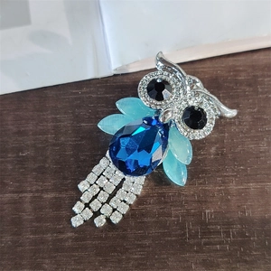 Close-up of owl brooch with blue crystal body and rhinestone tassels on wood surface