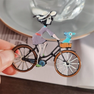 Vue à la main d'une broche en émail d'une fille à vélo avec un petit chien dans le panier