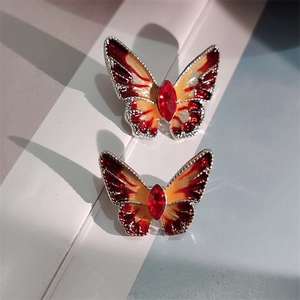 Detail van twee zilveren vlinderbroches met rood-oranje emaille verloop en kristallen