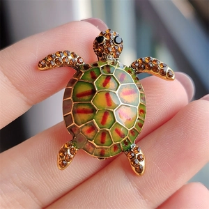 Detail of a turtle brooch with green enamel and amber rhinestones held in hand
