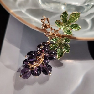 Detailed view of grape cluster brooch with purple beads and green leaves on ceramic surface