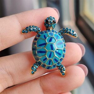Detail of creative turtle brooch with blue enamel shell and rhinestones held in hand