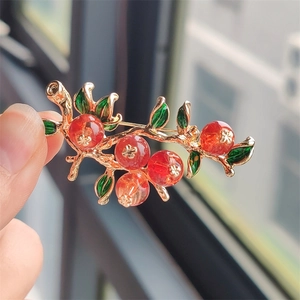 Detailed close-up of a pomegranate brooch with red resin beads and green enamel leaves