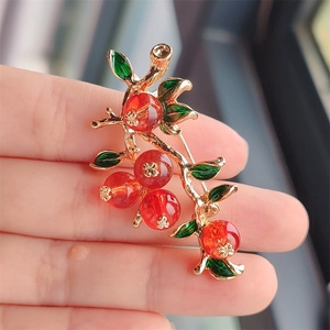 Detailed view of Persimmon brooch featuring red beads and golden branches on a hand